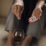 Woman’s hands mixing pills into a glass of red wine