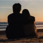 A couple hugging and sitting on the beach at sunset