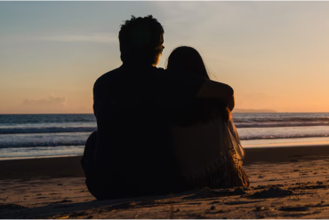A couple hugging and sitting on the beach at sunset