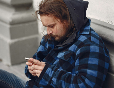 A man in blue checked flannel shirt looking at his phone searching for cocaine addiction treatment California