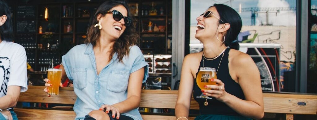 Two girlfriends laughing while drinking beer as a part of California sober lifestyle